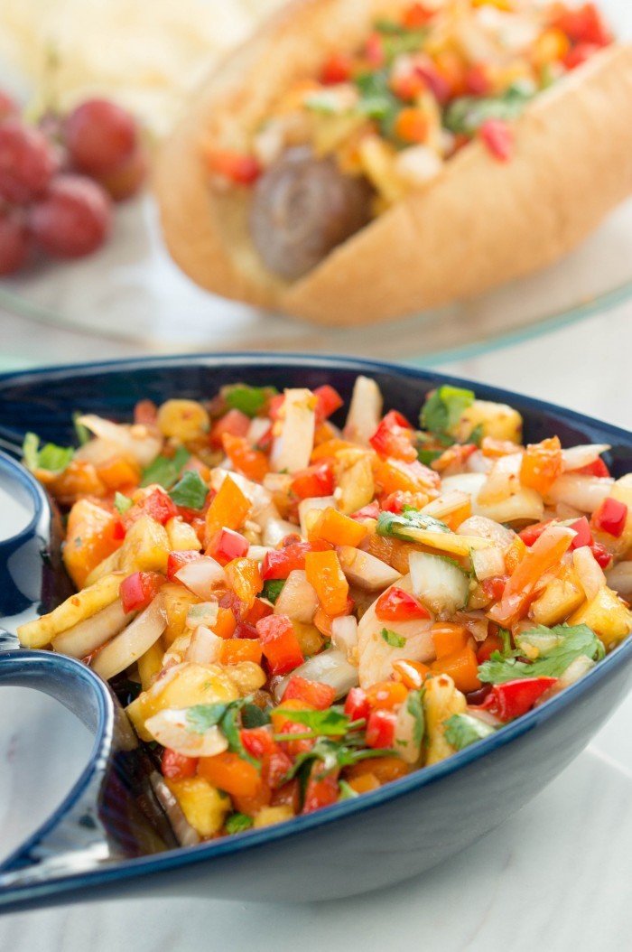 Bratwursts & Pineapple Relish Recipe 5 This pineapple relish will be the perfect garnish for all your favorite recipes! Serve it on top of brats, hamburgers, chicken, steak, or fish! Yummy side dish to add to your picnic or dinner recipe! If you're looking to make something special for dad this year, look no further than Bratwurst with pineapple relish garnish! It will fill his craving for meat and be a dinner he'll remember. You don't even have to head to the grill to pull off this amazing meal. This pineapple relish will be the perfect garnish for all your favorite recipes! Serve it on top of brats, hamburgers, chicken, steak, or fish! Yummy side dish to add to your picnic or dinner recipes! Bratwursts with a Pineapple Relish Garnish Pineapple Relish Recipe Bratwursts with Pineapple Relish Recipe Type: Sides Cuisine: American Author: Janel at A Mom's Take Prep time: 15 mins Total time: 15 mins Serves: 4 cups Ingredients 1 pineapple 1 red bell pepper 1 orange bell pepper 1 small onion 1/2 bushel cilantro 1/4 cup rice vinegar 1/8 cup soy sauce 1/3 cup hot sauce 1/2 cup sugar Juice from 1 lime Crushed red pepper, ground (to taste) Instructions Finely dice pineapple, bell peppers, and onion and add to a bowl. Coarsely chop cilantro, add to your bowl. Add vinegar, soy sauce, hot sauce and sugar. Juice one lime and add it to the bowl. Crush ground pepper with a mortar and pestal, than add it to your pineapple relish. Mix until well combined. Store in the fridge until ready to serve. Use as a relish to top your favorite meats. This pineapple relish will be the perfect garnish for all your favorite recipes! Serve it on top of brats, hamburgers, chicken, steak, or fish! Yummy side dish to add to your picnic or dinner recipes!